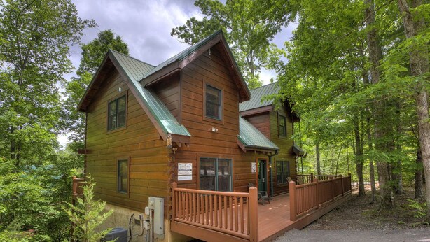 A cabin with a wooden exterior, a porch, and a metal roof, surrounded by trees. - GOT IT ALL U ALL  Pool Table , Arcade ,Hot Tub , Pools,Free WIFI,Pet Friendly ! (Sevierville)