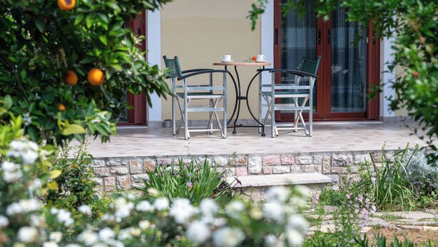 An outdoor seating area with two chairs and a table, surrounded by greenery and a stone wall. - Pappas Family House (Ναύπλιο)