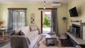 A living room with a sofa, coffee table, and a fireplace. There is a television mounted on the wall and a window with curtains. - Pappas Family House (Ναύπλιο)
