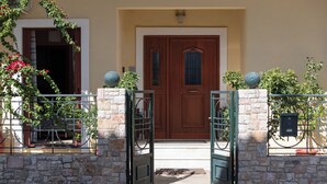 A stone-walled entrance with a wooden door, a metal gate, and potted plants. - Pappas Family House (Ναύπλιο)