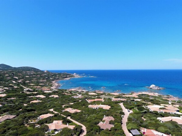 Vista aérea de una zona residencial costera con casas, calles y un mar azul cristalino.