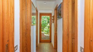 A hallway with wooden doors, a tiled floor, and a view of greenery outside. - Maximilian by Interhome (Portobello)