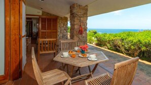 A wooden table with chairs on a patio with a stone pillar and a view of the ocean. - Maximilian by Interhome (Portobello)