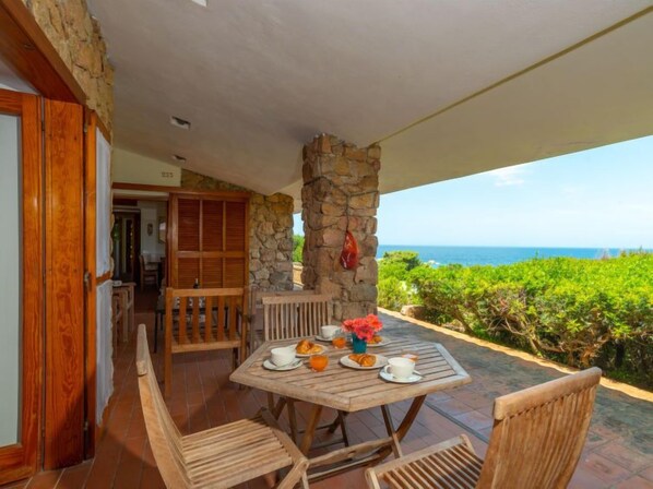 A wooden table with chairs on a patio with a stone pillar and a view of the ocean.