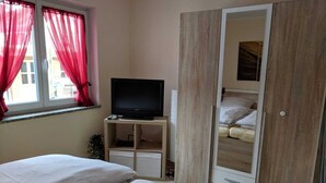 Quarto com duas camas, uma televisão sobre um suporte e um guarda-roupa.
