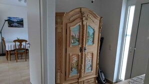 Quarto com um guarda-roupa de madeira grande, uma mesa de jantar com cadeiras e um aspirador de pó.