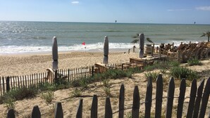 A beach with a wooden fence, lounge chairs, and a flag on the sand. - House 6/8 pers in holiday resort - pine forest, ocean, lake, your choice! (Lacanau Océan)