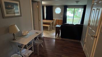 Un espace de vie compact comprenant un coin repas, un canapé, une petite table avec une lampe et une poubelle.