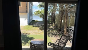 A patio with wicker chairs and a small table, a grassy yard, a wooden fence, and a view of a body of water.