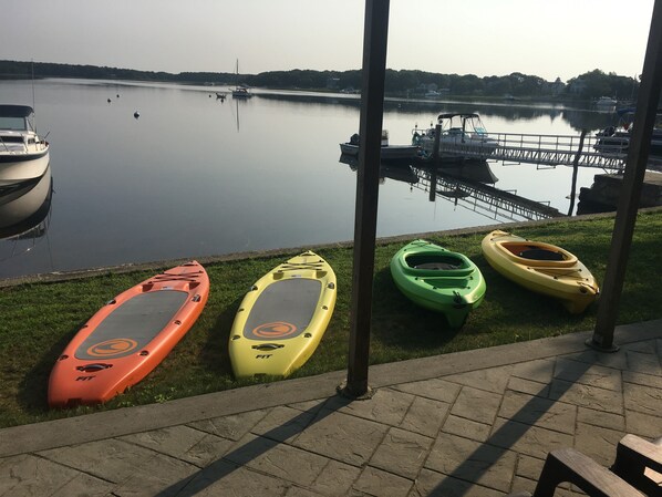 A calm lake with kayaks lined up on the grass near the water's edge.