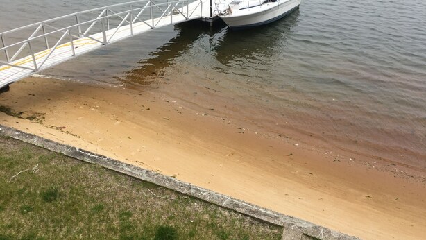 Um barco atracado num cais de betão, com uma praia arenosa ao fundo.