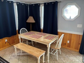 A dining area with a wooden table, two chairs, a bench, and a window with curtains.