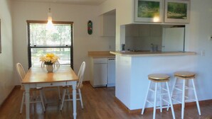 Una cocina con una mesa de comedor, sillas, una pequeña isla con taburetes, lavavajillas y una ventana con persianas.