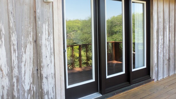 Fachada de madera con puertas de vidrio enmarcada en negro que dan a un balcón.
