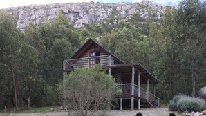 Two donkeys in a grassy area with a wooden cabin and a cross on a hill in the background. - Damiro (Piriapolis)
