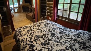 A cozy log cabin room with a bed, a fireplace, and a view of the outdoors. - Damiro (Piriapolis)