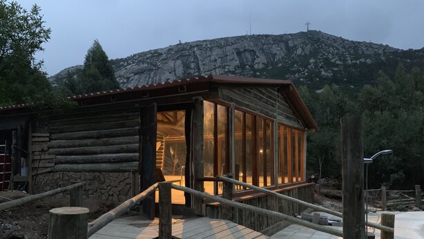 A rustic wooden cabin with a glass door, a wooden deck, and a mountain backdrop. - Damiro (Piriapolis)