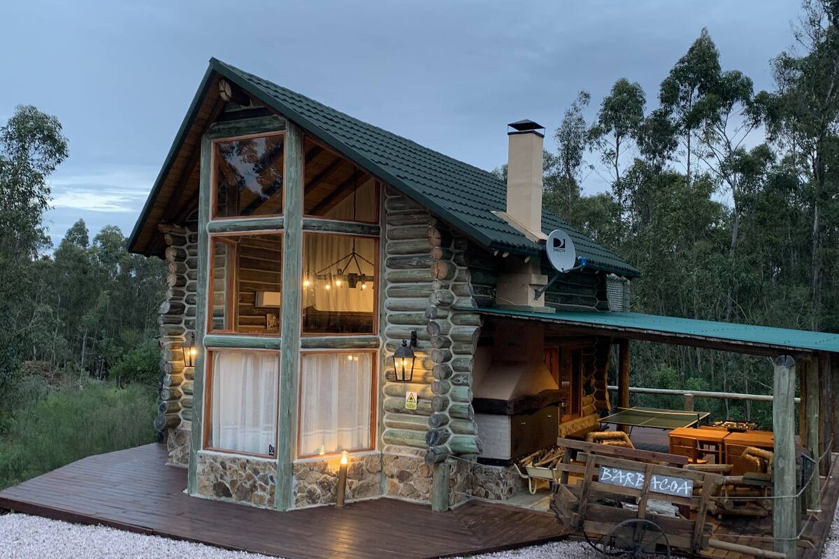A log cabin with a large window, a fireplace, and a deck.