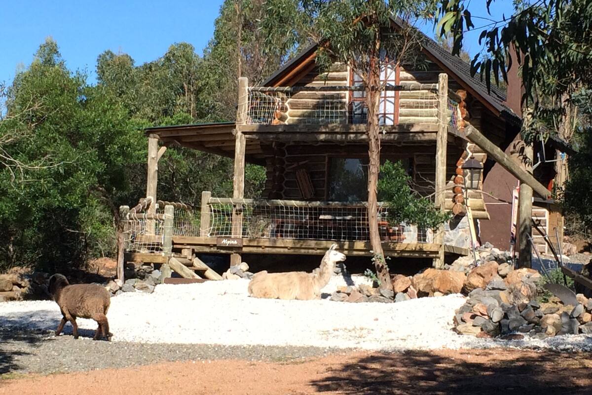 A rustic log cabin with a wooden deck and a fenced enclosure for animals.
