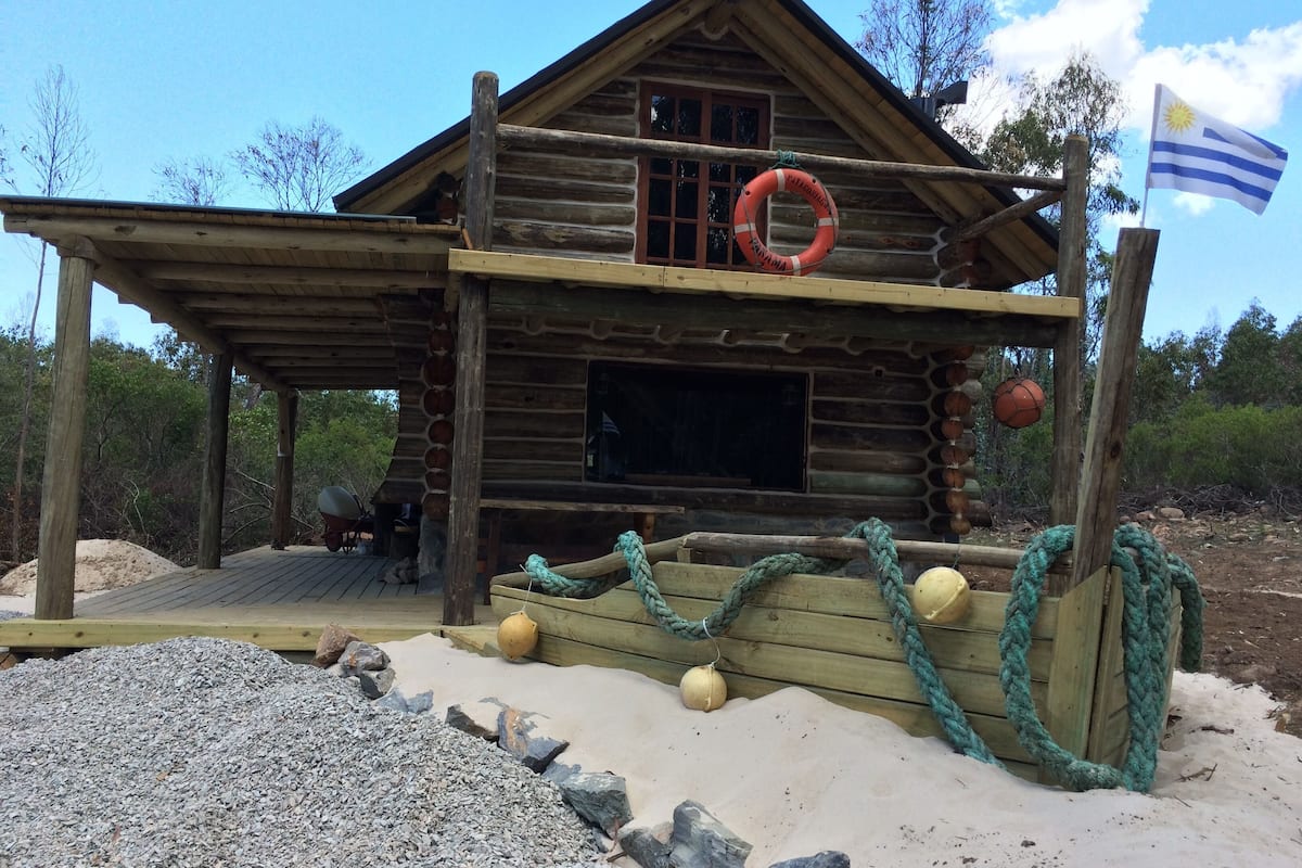 A wooden cabin with a covered porch, a lifebuoy, and a flag.