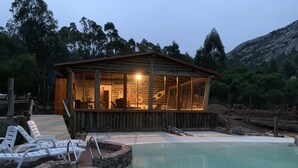 A wooden cabin with a glass enclosure, a swimming pool, and a wooden deck with lounge chairs. - Damiro (Piriapolis)