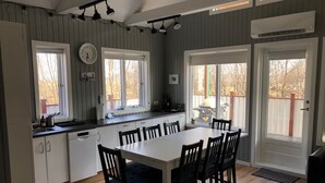 Une cuisine avec une table et des chaises blanches, des armoires en bois et une fenêtre donnant sur une terrasse.