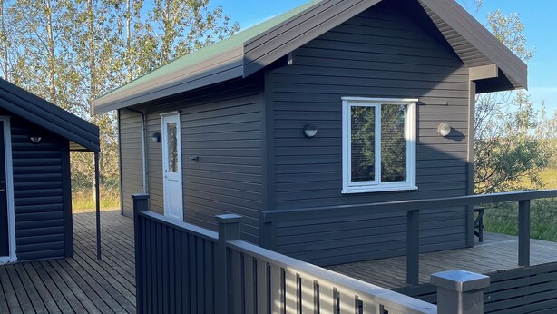 Une cabane moderne dotée d’une terrasse, d’une porte et d’une fenêtre.