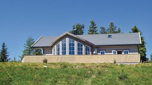 A modern two-story house with large windows, a sloped roof, and a wooden deck.