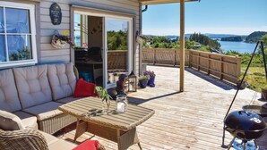 A covered deck with a sofa, table, and grill, overlooking a lake.