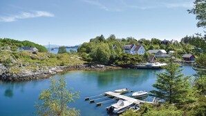 A coastal village with houses on a hillside overlooking a calm bay with boats docked at a pier.