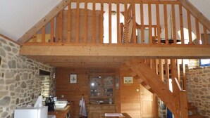Un interno in legno con una parete in pietra, una scala di legno e un angolo cottura con lavello e pensili.