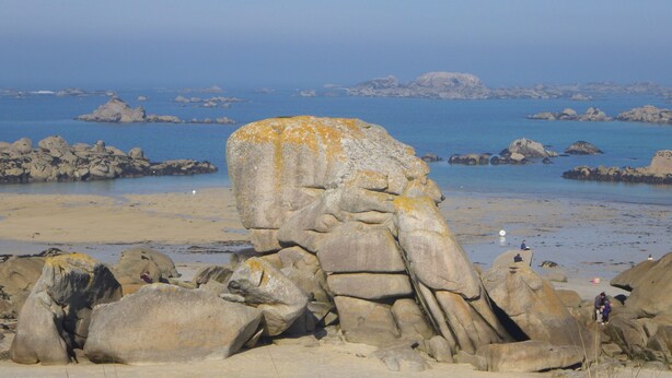 Paesaggio costiero roccioso con grandi massi e una spiaggia sabbiosa.
