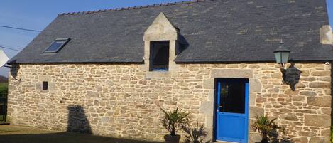 A stone building with a sloped roof, a small window, and a blue door.