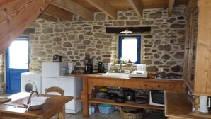 Una cucina rustica con pareti in pietra, un tavolo di legno, una lavatrice e un lavandino.