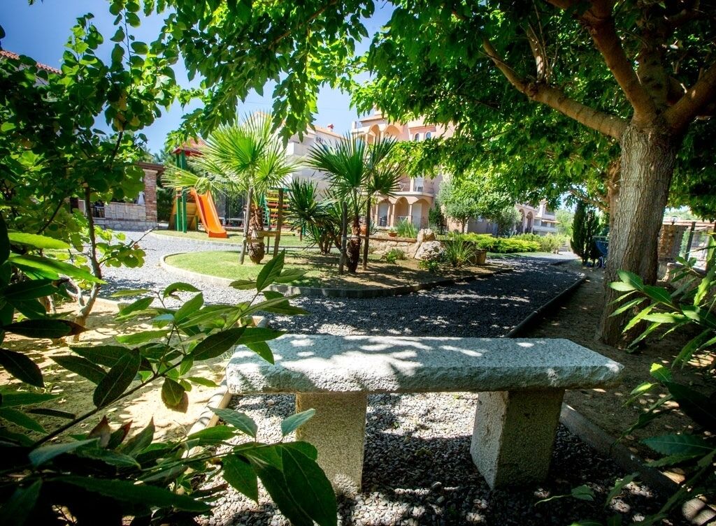 Une cour avec un banc en pierre, des palmiers et une aire de jeux.