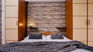 A bed with a grey knitted blanket, a headboard with a grid pattern, and wooden cabinets with a light fixture on the wall.