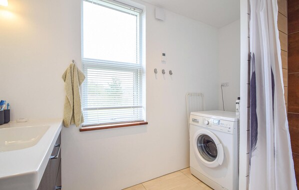 A compact laundry room with a washing machine, a drying rack, and a window with blinds.
