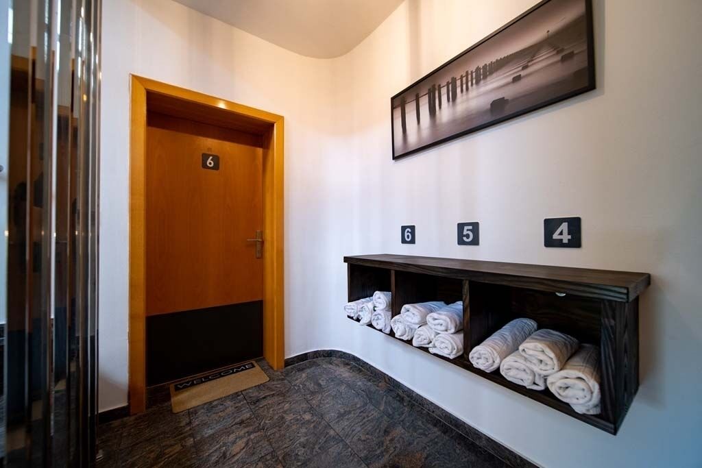 A hotel lobby with a wooden door marked '6', a wall-mounted towel rack with towels, and a framed picture above the rack.