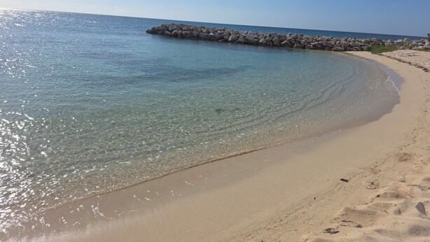 Ein sauberer Strand mit einem steinernen Wellenbrecher und ruhigem Wasser.