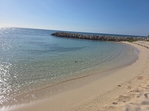 A clear beach with a rocky breakwater and calm waters.