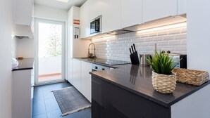 A modern kitchen with white cabinetry, a black countertop, and a built-in microwave. - Beny's Beach House - 2 min walk to the rock beach (Portimão)