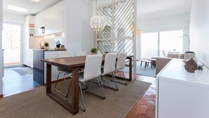 A modern dining area with a wooden table and white chairs, a kitchen in the background, and a decorative globe light. - Beny's Beach House - 2 min walk to the rock beach (Portimão)