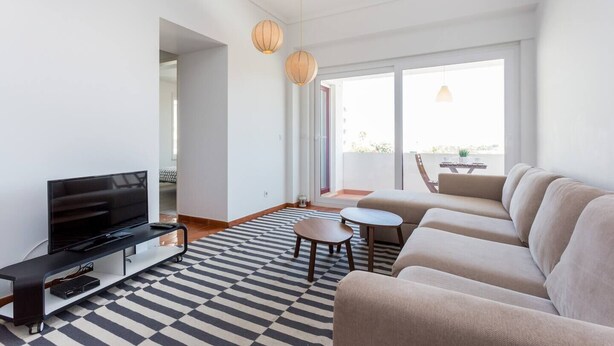 A modern living room with a flat-screen TV, a sofa, a coffee table, and a patterned rug. - Beny's Beach House - 2 min walk to the rock beach (Portimão)