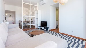 A modern living room with a sofa, TV, and a partition with a herringbone pattern. - Beny's Beach House - 2 min walk to the rock beach (Portimão)