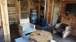 Interior acogedor de una cabaña con paredes de madera, chimenea de piedra y dos sillones de madera con mantas de piel.