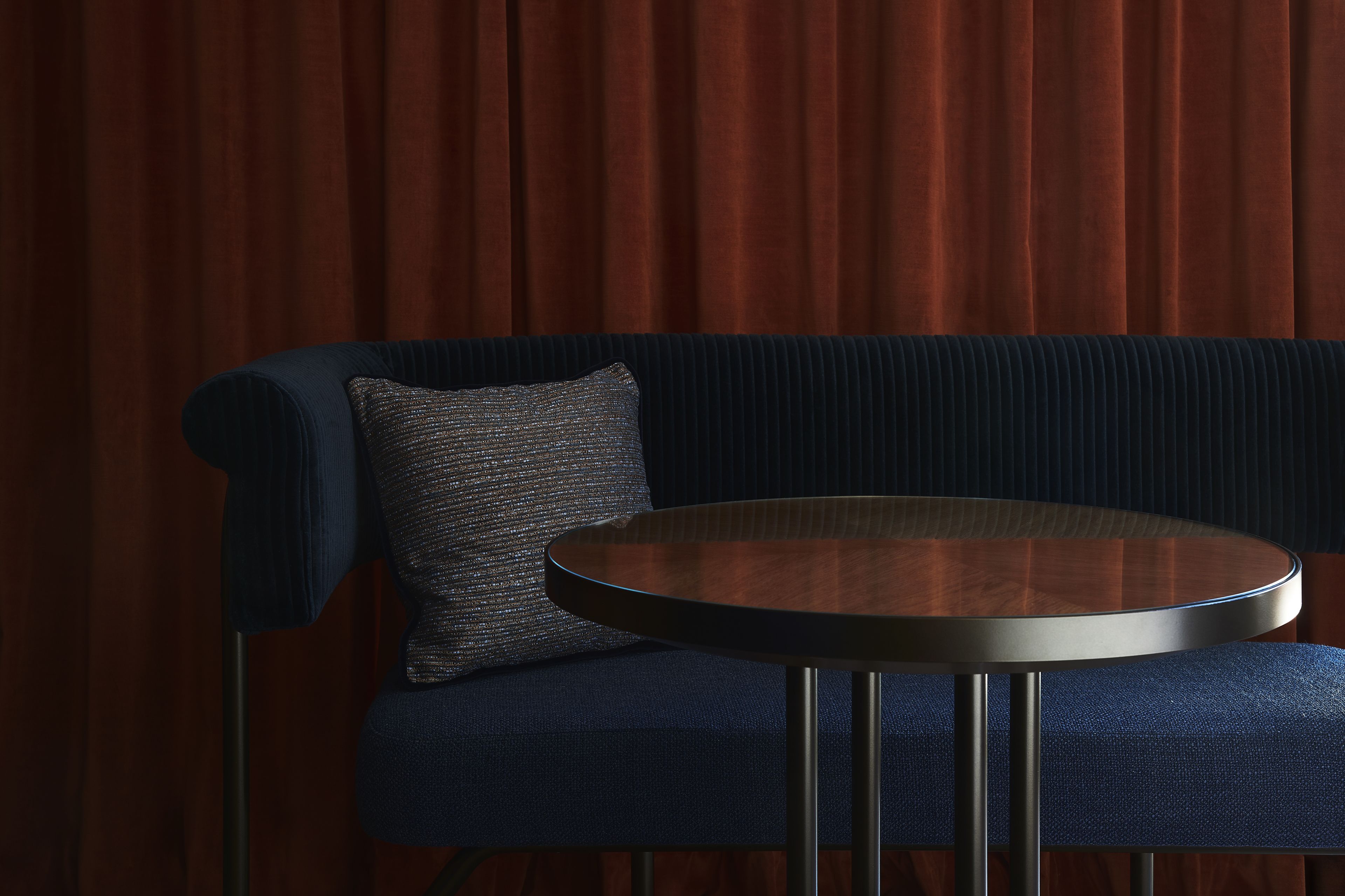 A dark blue sofa with a textured pillow and a round table with metal legs.