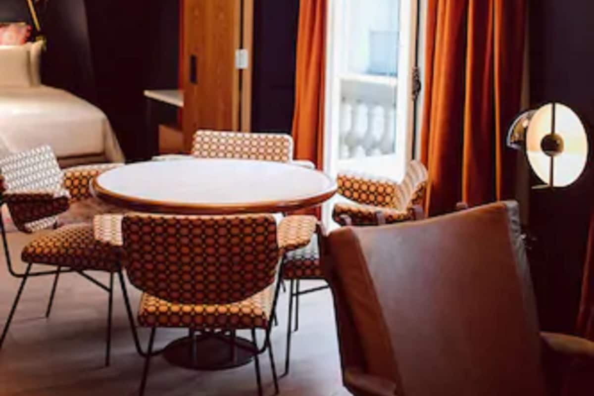 A hotel room with a round dining table, two chairs, a sofa, a lamp, and a bed.