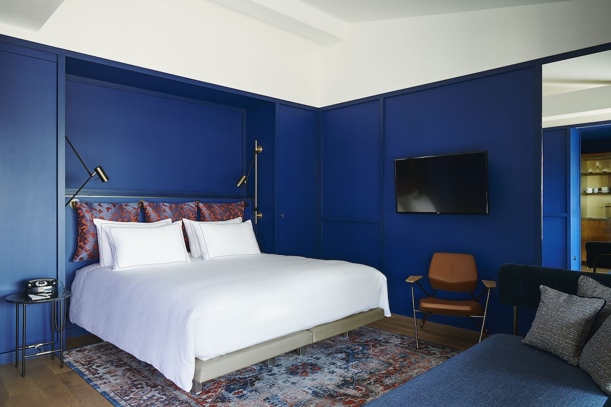 A bedroom with a large bed, a chair, a TV, and a small table.