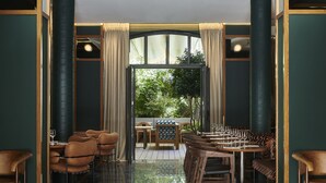 A restaurant with a high ceiling, dark green walls, and a polished black marble floor. There are multiple tables and chairs arranged for dining. - Hotel Le Ballu (Paris)