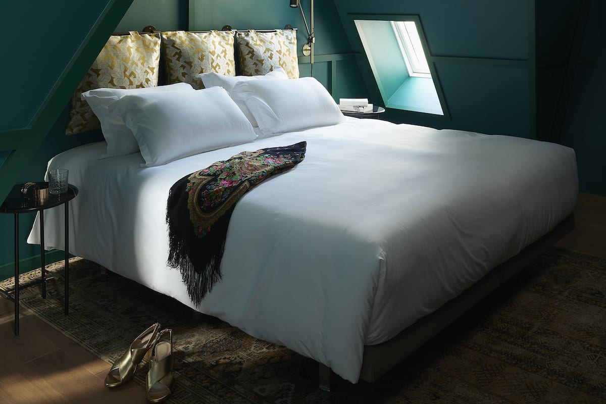 A bedroom with a large bed, a small side table, a lamp, and a window with a view.